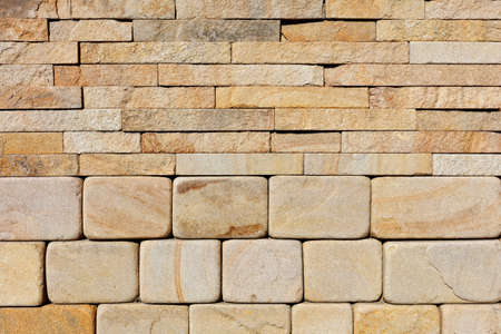 The background and texture of a wall composed of hewn rounded yellow sandstone at the base and rough...