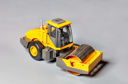Toy model of construction vibrating roller in yellow color on light gray background, selective...