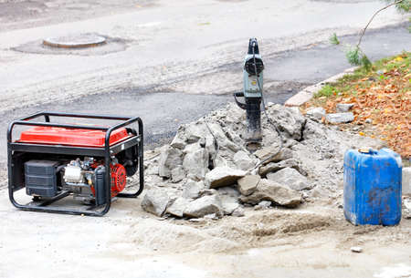 Electric jackhammer with a gas generator, a blue can of gasoline on the background of a workplace with a road section being repaired, copy space.の写真素材
