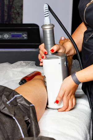 A professional beautician performs an electromagnetic massage of the muscles in the leg using a...