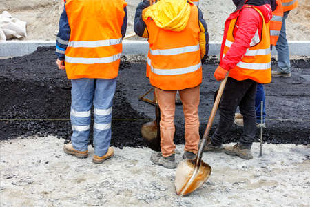 A working group of road workers in orange overalls got together to discuss a work plan for paving the section of the road with fresh hot asphalt. Copy space.の写真素材