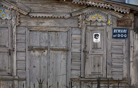 Old dilapidated wooden facade of the house with carved platbands, curly wall elements and metal bars, with a sign Beware of dog.の写真素材