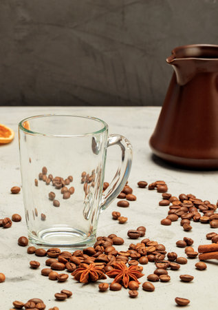 A transparent glass cup and a coffee turk surrounded by coffee beans, anise stars and cinnamon sticks against a gray concrete background. Vertical image, copy space.の写真素材