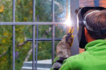 A bright flash from an electrode when a welder works to install a metal fence around a house against...