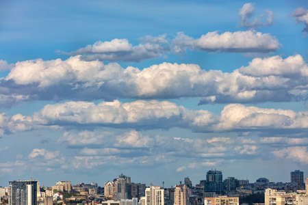Cityscape with white clouds hovering over the city in the blue sky and casting shadows under the sun's rays. Copy space.の写真素材