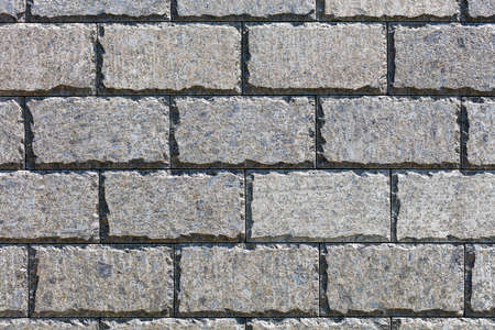 The chipped edges of a smooth rectangular stone tile of polished rough stone, illuminated by sunlight, create a pleasing symmetrical pattern on the wall surface. Copy space, high resolution.の写真素材