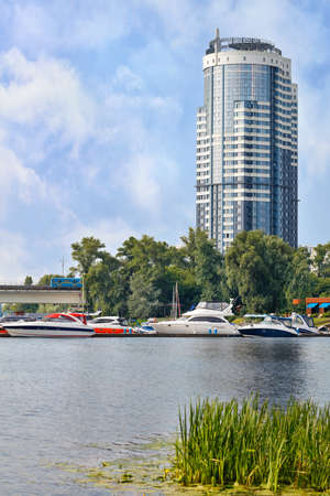 Summer landscape with modern residential building, subway train and pier with boats on the river bank on a sunny summer day. Vertical image, copy space.の写真素材