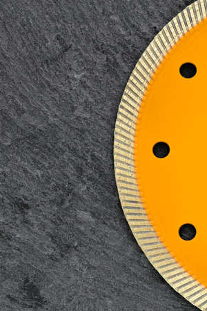 Part of diamond cutting wheel with thin cutting segments for cutting stone and granite, yellow circle on dark gray granite background, copy space. Vertical image.の写真素材