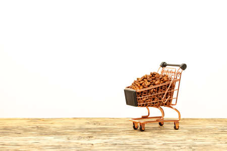 Coffee beans are poured with a slide into a shopping cart, standing on a wooden surface against a light beige background. Close-up, copy space.の写真素材
