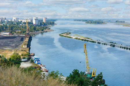 The bay of the river industrial port for the supply of coal to the city's thermal power plant against the backdrop of a wide river, cloudy sky and cityscape.の写真素材