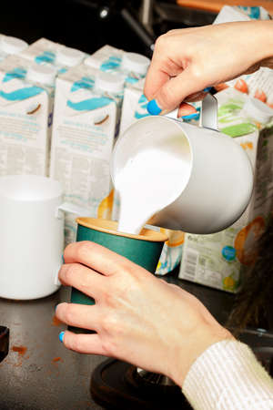 Close-up shot of a barista adding frothed milk to coffee in a paper coffee cup.の写真素材
