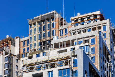 A fragment of the construction of a multi-storey residential building with facade insulation and finishing with metal-plastic panels. Blue sky background, copy space.の写真素材