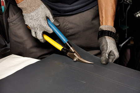 The male hands of a worker cut a sheet of roofing iron with metal scissors for subsequent waterproofing of the roof. Close up, copy space.の写真素材