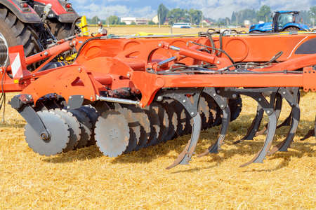 A multirow disc harrow with loosening blades is mounted on a tractor against a background of yellow...