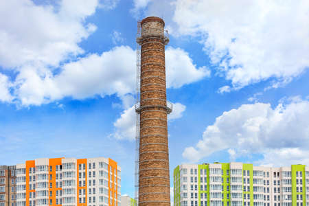 The old high brick chimney of the thermal power plant stands in the middle and rises above the new...