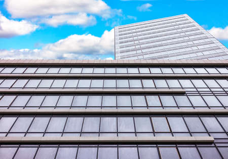 City business center, a building made of glass and concrete against a cloudy blue sky.