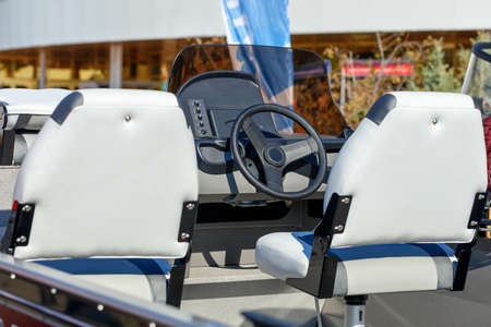 The steering wheel on the captain's bridge between the white leather seats of the riverboat.