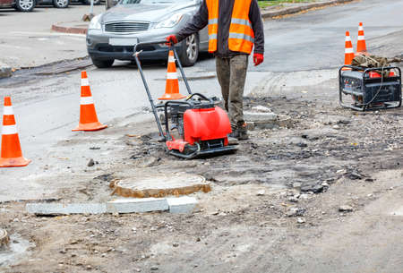 A road service worker rams a section of the carriageway fenced with orange traffic cones near sewer...