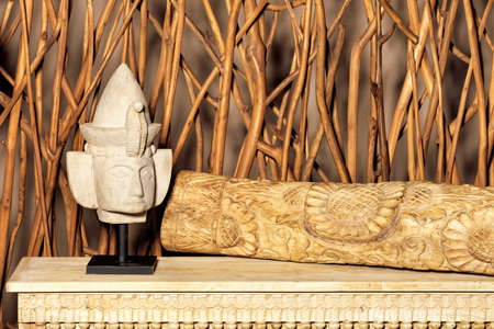 Gypsum figurine of the head of a sphinx with a carved wooden trunk on a wooden table.の写真素材