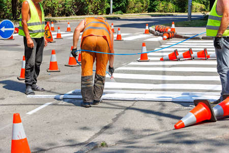A team of road workers on a fenced section of the carriageway with a paint sprayer mark white road markings for a pedestrian crossing. copyspace.の写真素材