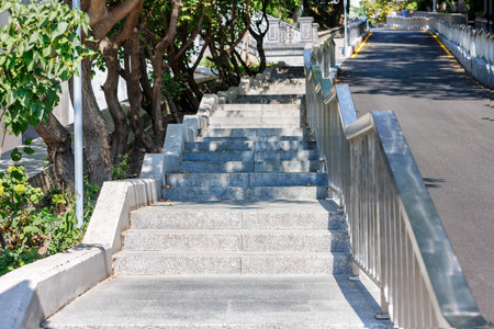 Granite steps of a stone staircase are located along an asphalt road in a modern city park on a...