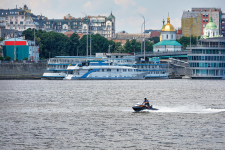 A middle-aged man in shorts, a T-shirt, a helmet and a life jacket rides a black water scooter along...