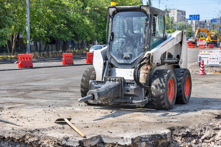 A small and manoeuvrable construction vehicle with an attached jackhammer is parked in a...