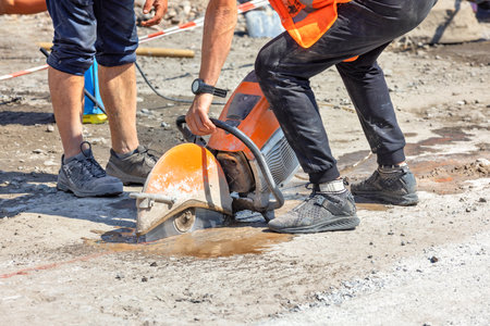 A petrol circular cutter in the hands of a worker cuts the asphalt c oncrete road surface on a sunny summer day. Copy space.の写真素材