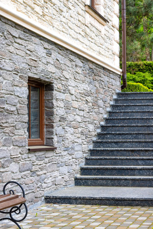 Granite steps along the stone wall of the house with a window leading to the green garden in the background. Vertical image.の写真素材