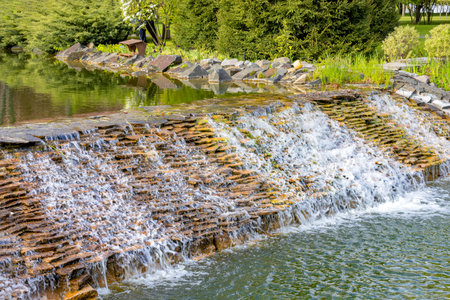 A beautiful artificial waterfall in a summer pond in the landscape design of a summer park.の写真素材