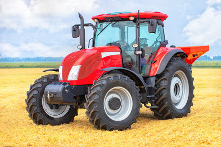In a sprawling wheat field under a blue sky, a red tractor displays powerful modern agricultural machinery conceptの写真素材
