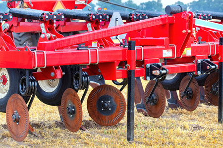 Close-up of farming equipment with red plow, showing agricultural machinery on field with steel disc harrows, rural farming conceptの写真素材