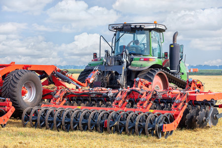 A powerful tractor equipped with modern tilling equipment engages in agricultural activities, efficiently preparing the field for planting. The landscape showcases lush greenery and a vibrant sky.の写真素材