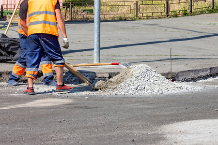 Construction workers in bright vests are busy repairing a city street, applying fresh concrete to a section of pavement under a clear blue sky, showcasing teamwork and dedication. Copy space.の写真素材