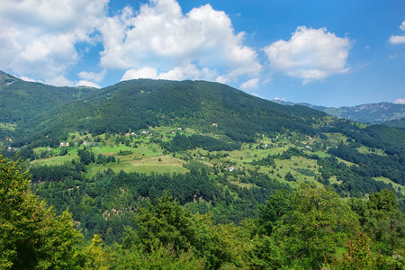 Rolling hills display vibrant greenery and patches of trees, creating a tranquil landscape. Fluffy clouds drift lazily above in the clear sky, capturing the peaceful essence of rural scenery.の写真素材