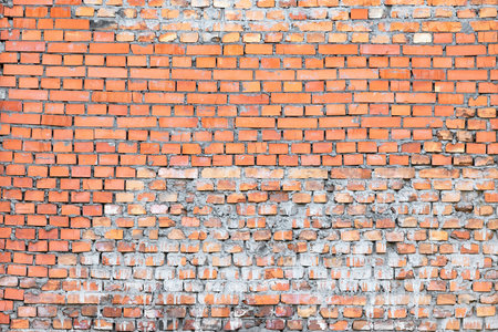 A weathered brick wall displays a blend of orange and gray hues, revealing its history through a unique texture. Sunlight casts gentle shadows, highlighting the imperfections of each brick.の写真素材