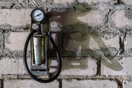 A foot pump for pumping tires. A pump with a gauge hangs on a gray brick wall.の写真素材