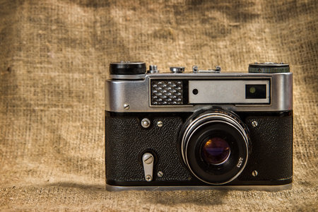 An old film camera against a burlap background. analog mechanical camera. range finder camera.