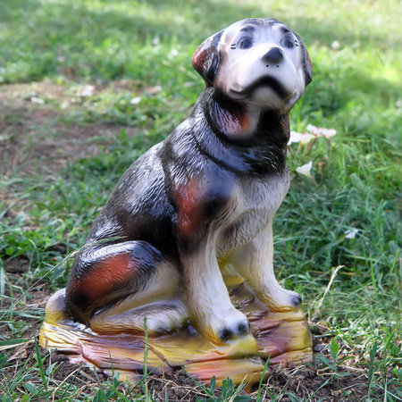 Ceramic figurine of a dog. A toy dog sits on the grass in the garden.の写真素材