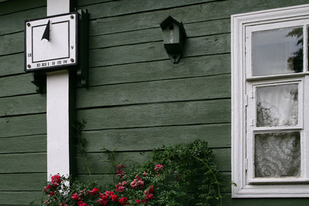 Wooden wall and window with red flowers in front of it.