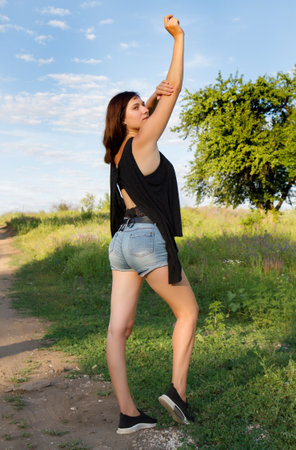 Girl in nature on a summer day. A girl in denim shorts rejoices in the sun and does a sports exercise.の写真素材