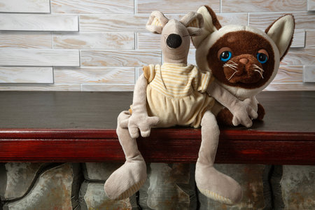 Teddy bear sitting on wooden shelf in front of white brick wall. Toy cat and mouse.