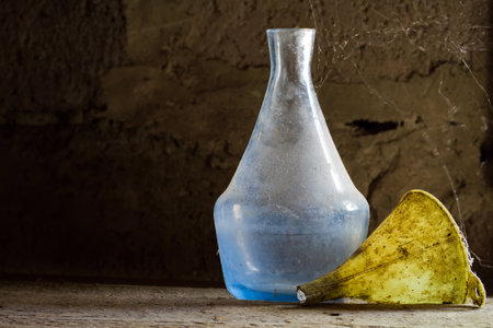 Antique dishes on a dusty wooden shelf. An old dirty bottle and funnel. An old glass bottle in a spider's web.の写真素材