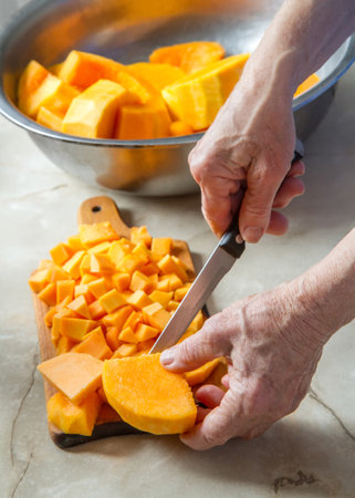 Slicing pumpkin in the kitchen. Hands of an elderly woman.の写真素材