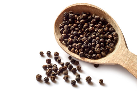 Black peppercorns on a white background. Wooden spoon with black peppercorns. Fragrant spices...