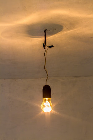 An old incandescent light bulb. A light bulb turned on in an old room.