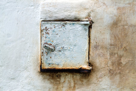 An old iron stove heating door. The door is in the plastered wall.