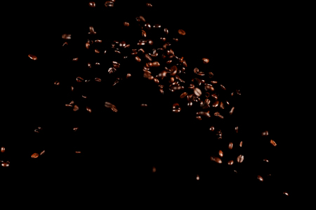 Flying coffee beans isolated on black background. Roasted coffee grains explosion.の写真素材