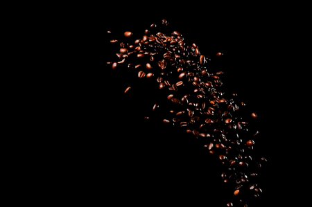 Flying coffee beans isolated on black background. Roasted coffee grains explosion.の写真素材