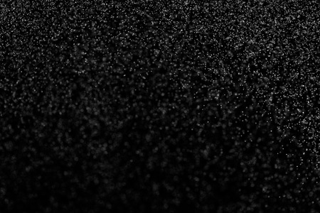 Abstract splashes of water on black background. Freeze motion of white particles. Rain, snow overlay texture.の写真素材